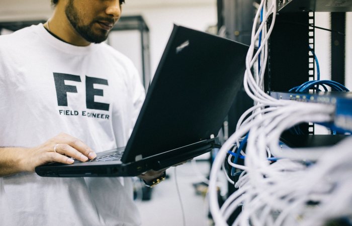 Crop focused Asian engineer in white shirt using modern netbook while working with hardware