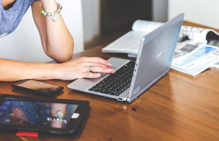Woman working remotely on a laptop with mobile devices on a wooden desk.