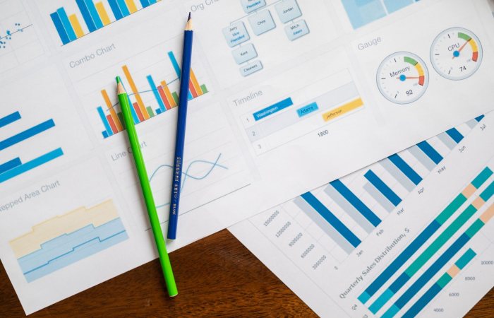 Flat lay of various business charts and colored pencils on wooden table, highlighting financial analysis.
