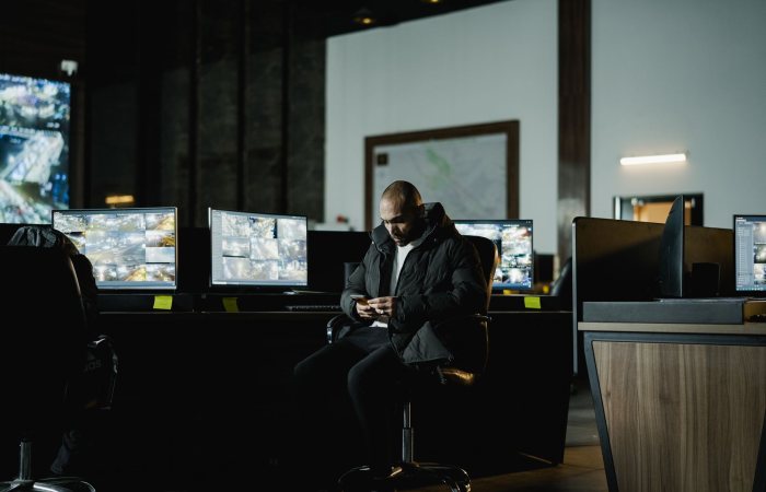 Security officer seated in a dimly lit control room, analyzing multiple surveillance screens.
