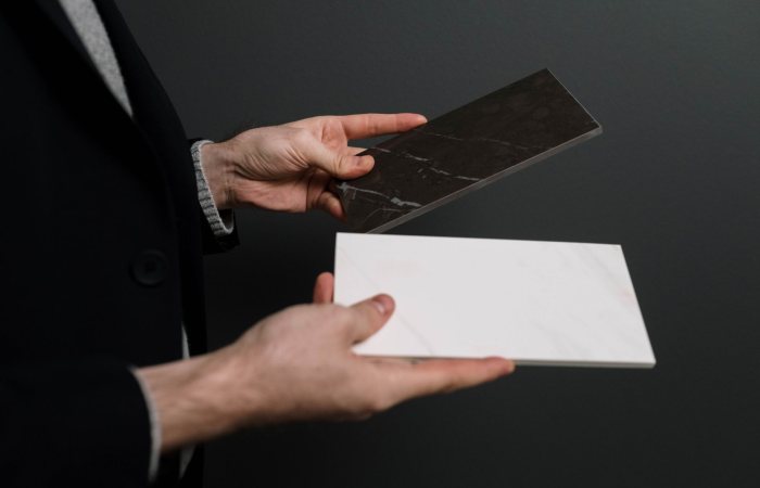 Close-up of hands holding two contrasting marble and stone tiles.