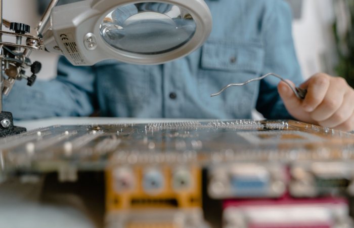 A detailed view of electronic circuit inspection using a magnifying glass and tools.