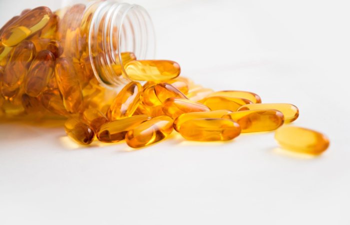 Close-up of fish oil capsules spilling from a bottle on white background.