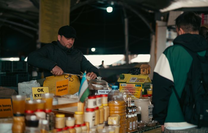 A vendor at an indoor market selling various honey jars. Captured in an atmospheric setting.