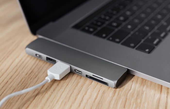 High angle of modern space silver laptop with USB type c multiport hub with plugged white cable placed on wooden table